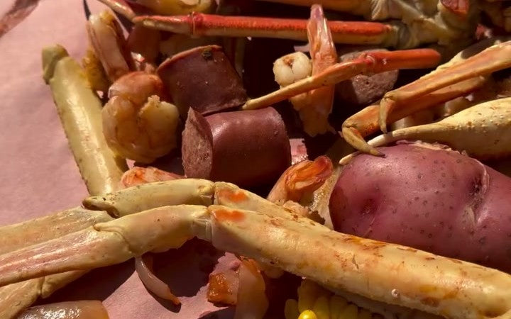 The seafood boil dumped on butcher paper: snow crab legs, shrimp, sausage, corn, red potatoes, and lemon.