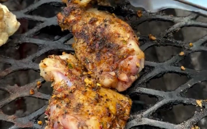 Marinated and rubbed chicken wings crisping over charcoal on an expanded metal grate.