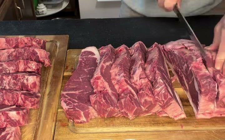 Thirteen New York strip steaks cut from one Black Angus strip loin, lined up on two boards in Pat's kitchen.