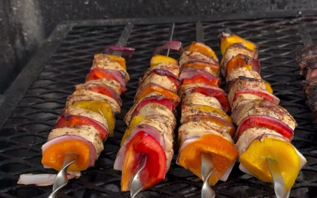 Steak and chicken kebabs with peppers and onion on the grate, a bottle of Chiavetta's Italian dressing in front.